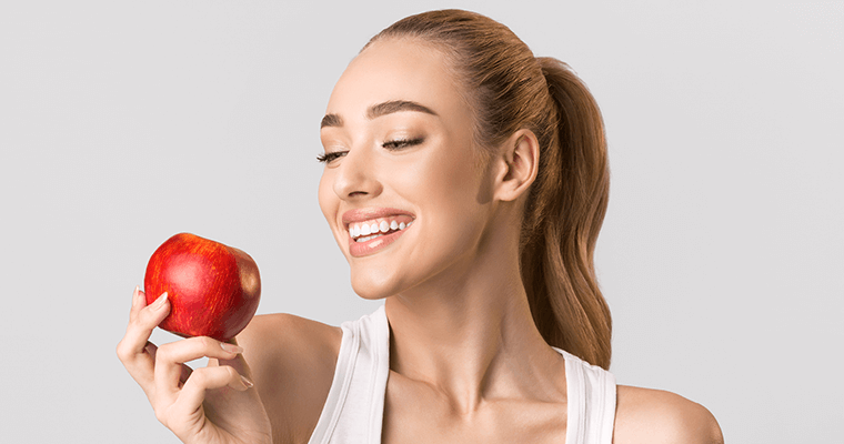 Smiling woman flashing her pristine teeth as she gazes at a red apple